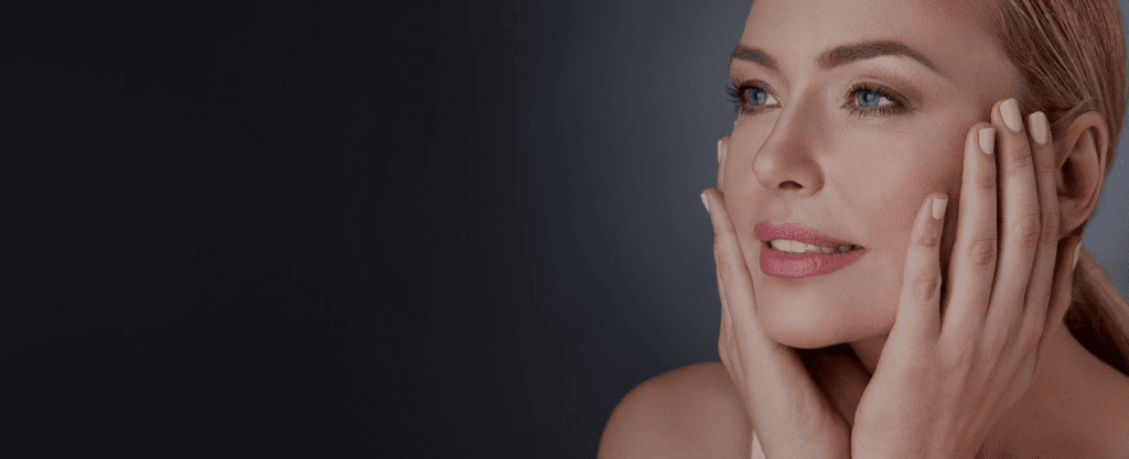 A woman smiles while gently touching her face, showcasing smooth and rejuvenated skin.