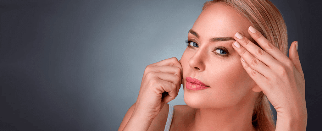 A woman gently pulling back the skin on her forehead to smooth wrinkles.