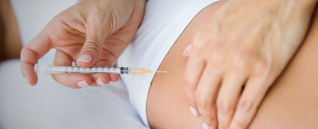 A close-up of a hand holding a syringe while administering an injection to the thigh.
