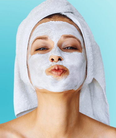 A woman wearing a white facial mask and towel, puckering her lips.
