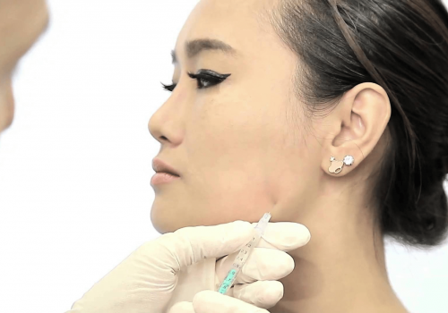 Practitioner administering an injection into a patient's jawline area.