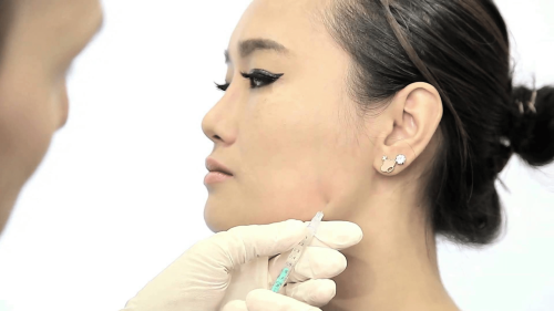 Practitioner administering an injection into a patient's jawline area.