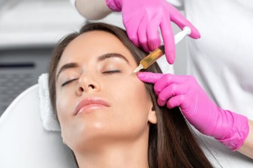 Practitioner in pink gloves administering a PRP injection to a patient’s face.
