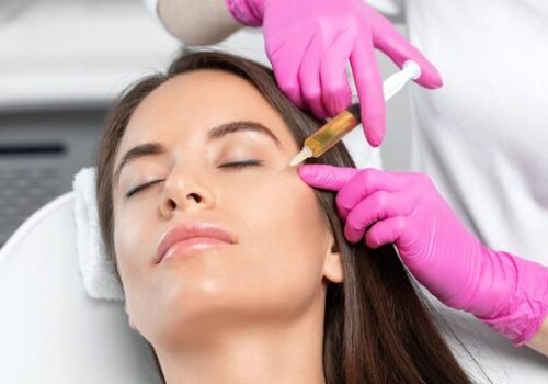 Practitioner in pink gloves administering a PRP injection to a patient’s face.