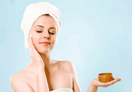 Woman with a head towel applying face cream.