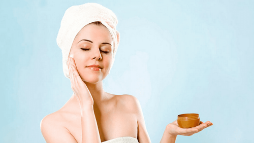 Woman with a head towel applying face cream.