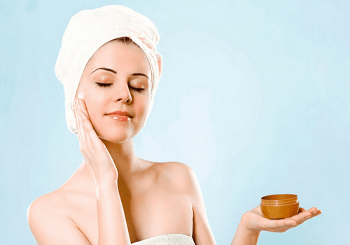Woman with a head towel applying face cream.
