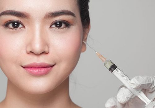 Professional holding a syringe near a patient's face for a dermal filler treatment