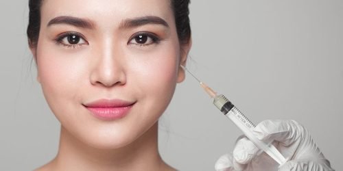Professional holding a syringe near a patient's face for a dermal filler treatment